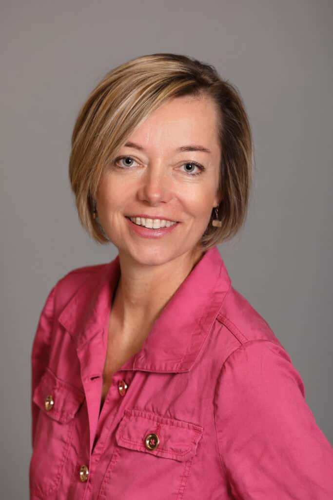 Portrait of a smiling woman with short blonde hair in a pink shirt.