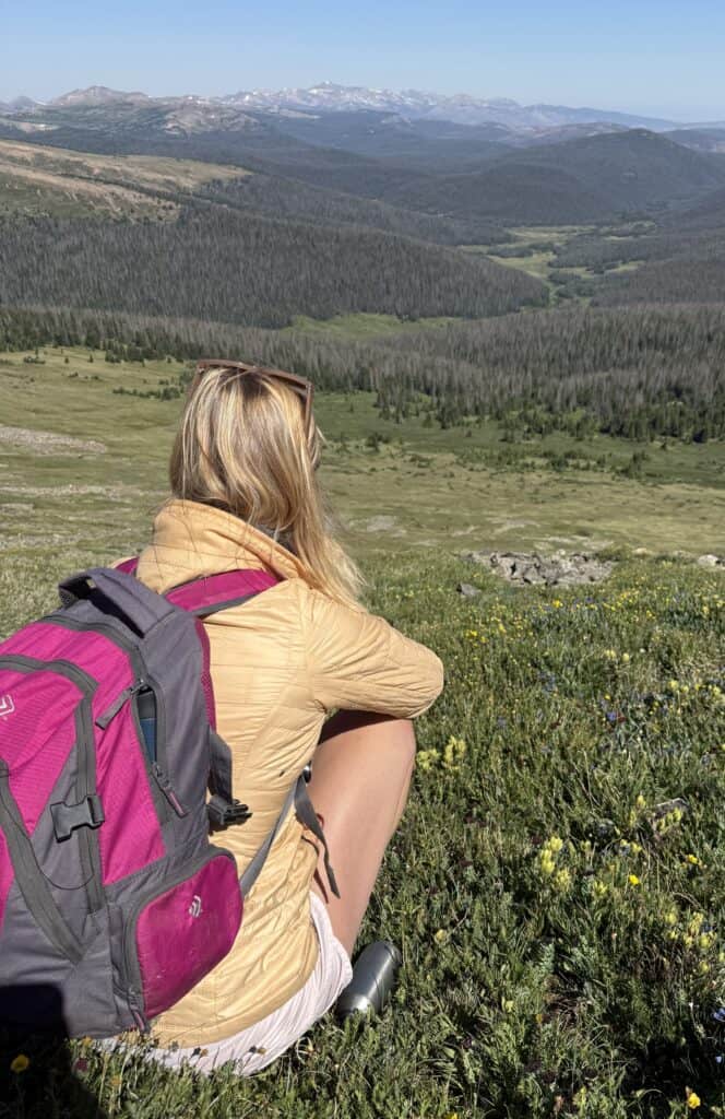 Hiker sitting on a mountain with panoramic view of mountains and forests.