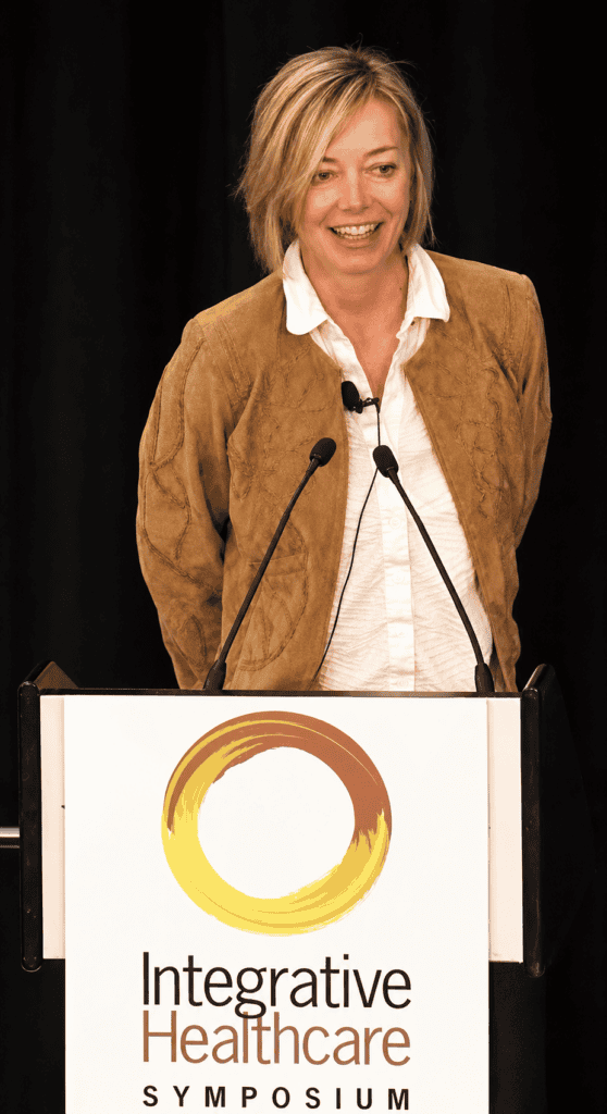 Woman speaking at a healthcare symposium with a podium and microphone.